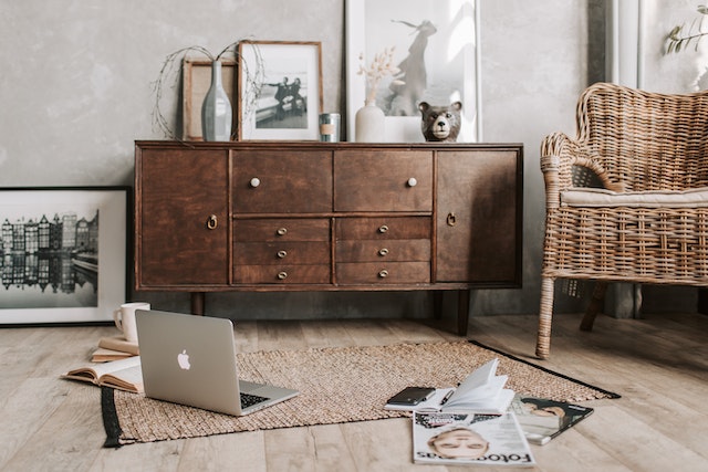 a room with a wicker chair, wooden drawers, and laptop on the floor